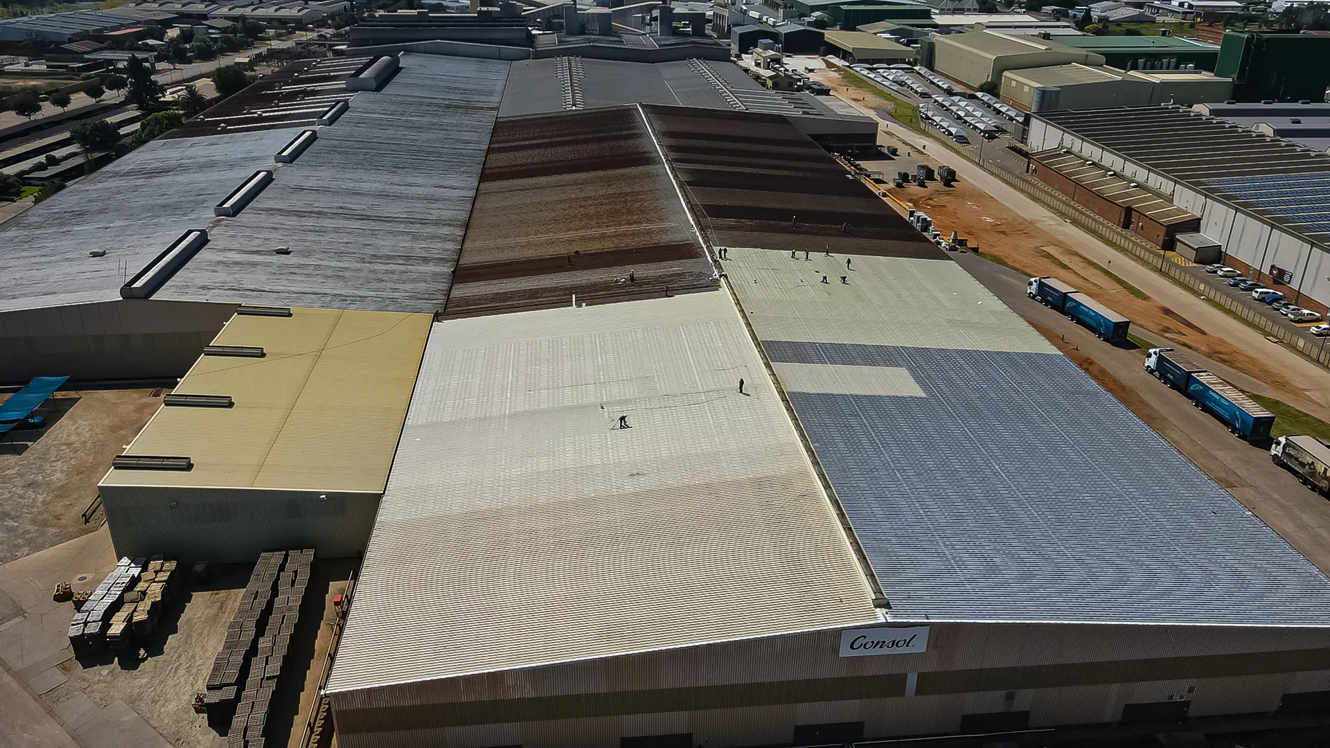 Aerial view of a large industrial complex, highlighting workers meticulously performing industrial roof cleaning on a Consol factory roof.